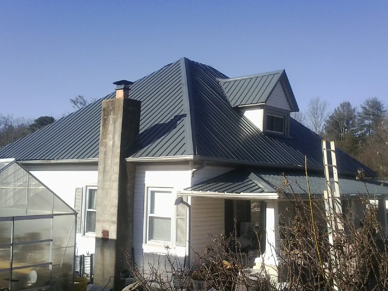 Dark blue standing seam metal roof on a white farmhouse with dormer — Slate & Tile Roof Repair by Roofing Brothers in Orfordville