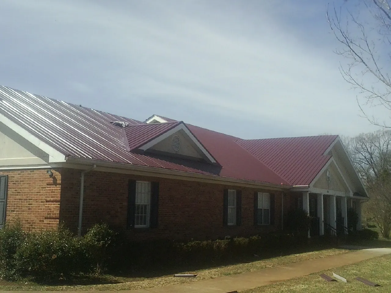 Red metal roof with gabled entries on a long brick building, from a Hail Damage Roof Repair job in Orfordville