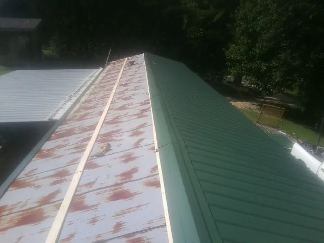 Old rusted panels beside newly installed green metal roofing — Wind Damage Roof Repair by Roofing Brothers in Orfordville