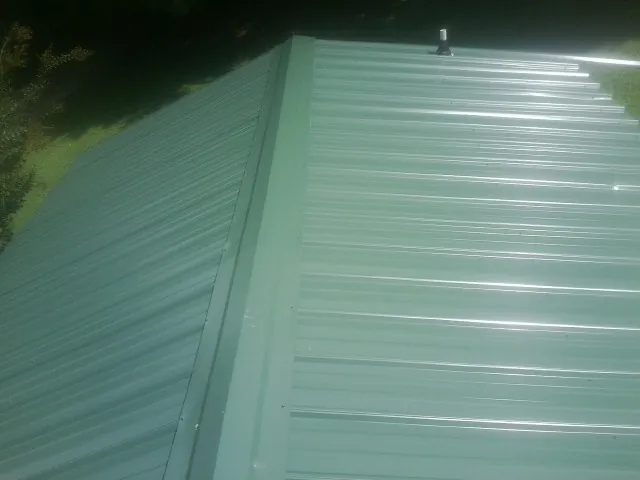New green metal panels meeting at the ridge of a roof — Flat Roof Repair work by our crew in Orfordville
