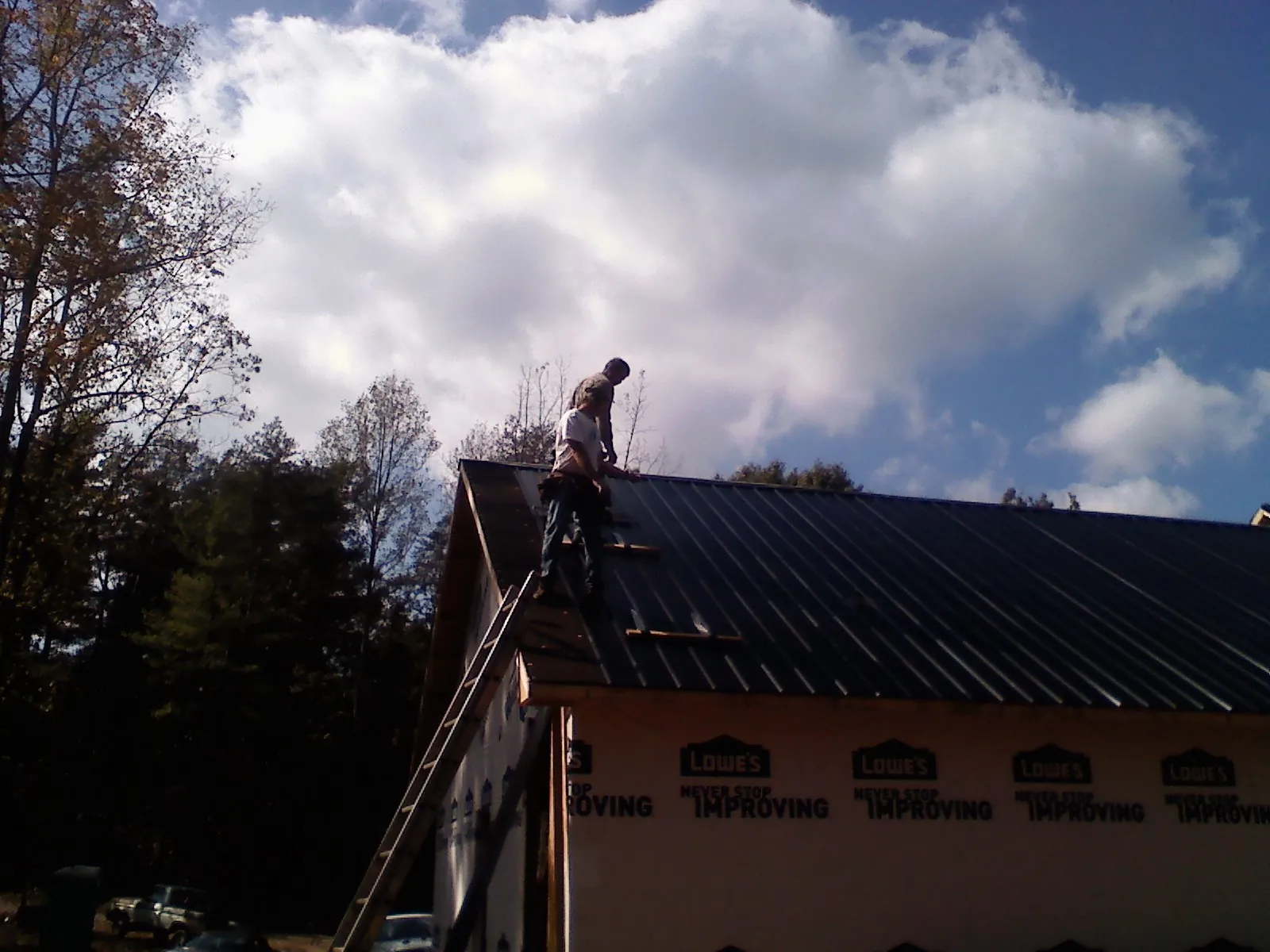 Roofer fastening dark metal panels high against a cloudy sky, from a Roof Inspection job in Orfordville
