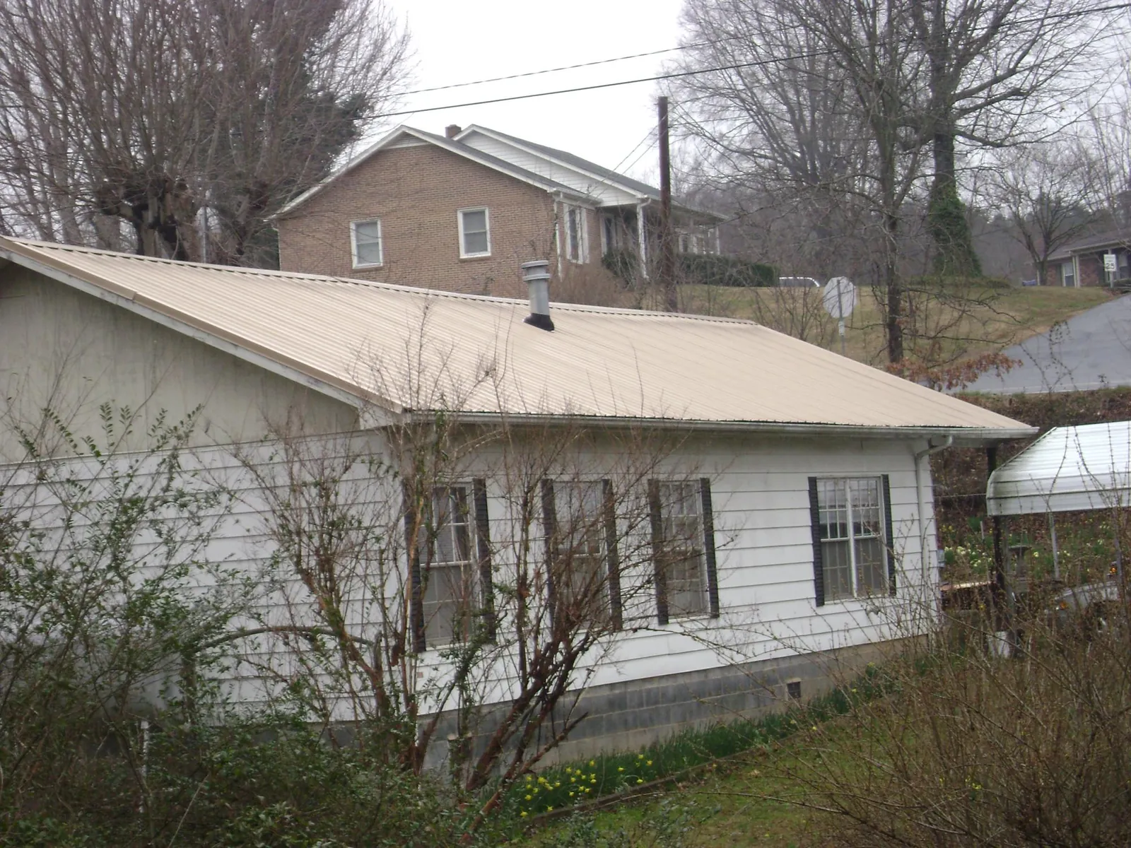 Tan metal roof on a white sided house set into a hillside — Commercial Roofing by Roofing Brothers in Orfordville