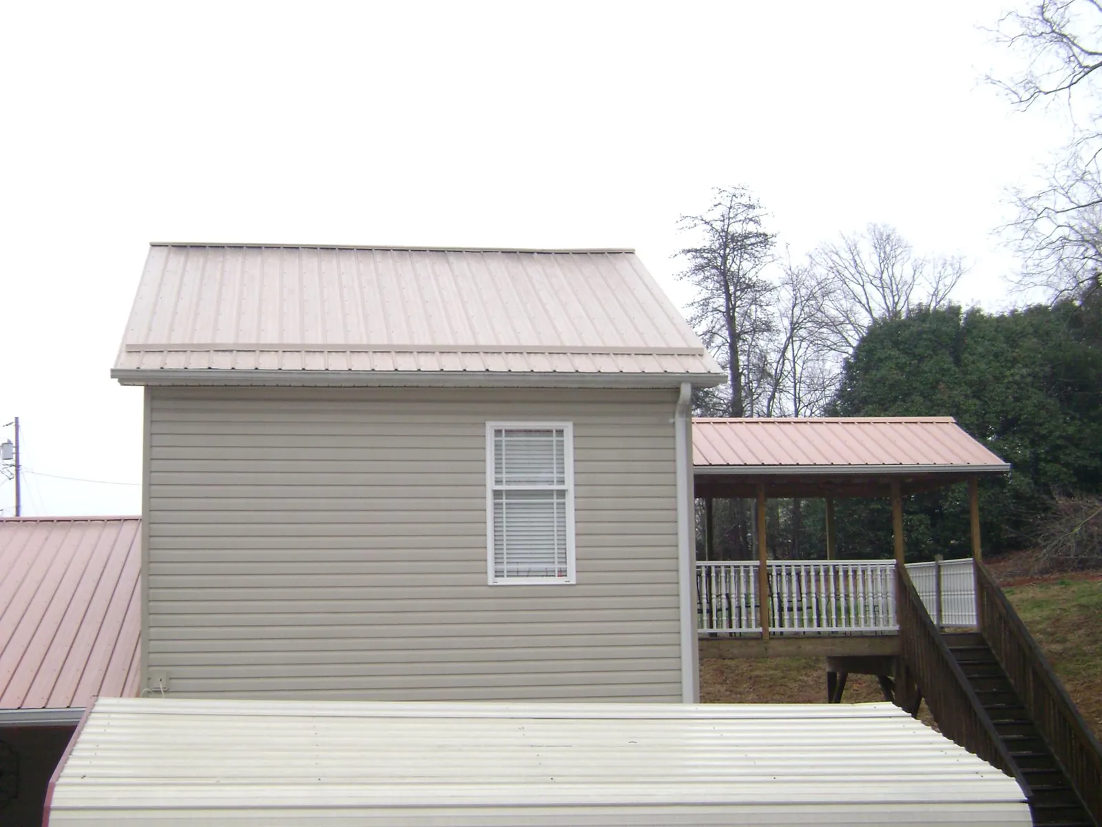 Tan metal roofs on a two story addition and attached porch, from a Roof Replacement job in Orfordville